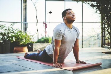Persona con camiseta gris y pantalones de chándal azul marino en posición de perro boca arriba, practicando un flujo de yoga de 20 minutos para una mejor movilidad
